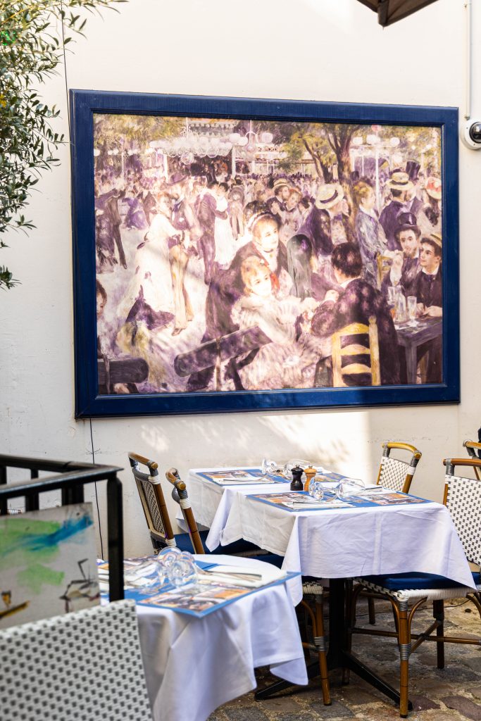 Photo de l'intérieur du restaurant avec des tables en premier plan et un tableau de Renoir en arrière plan.